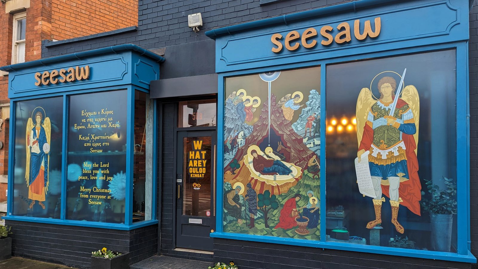 Seesaw Opticians shopfront displaying the completed Nativity window graphics with Greek and English Christmas greetings