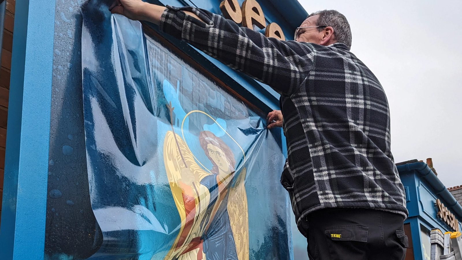 Installer applying an illustrated angel vinyl graphic to a Seesaw Opticians shop window